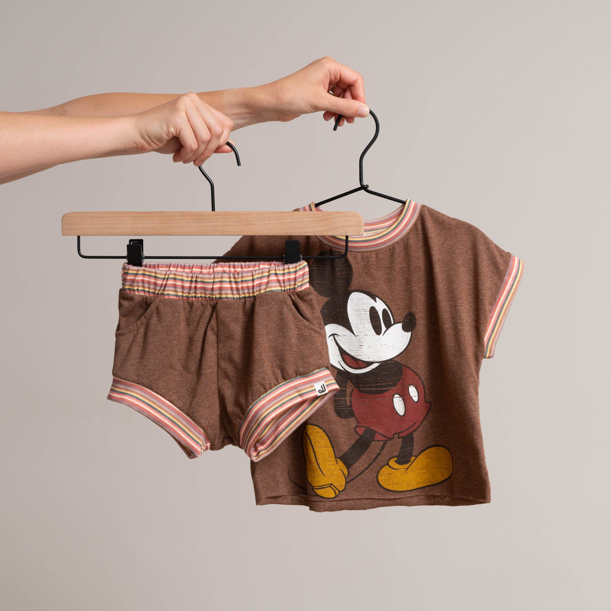 Hands holding a toddler children's Two-Piece Set of Vintage Mickey boxy t-shirt and shorts in brown and multicolor waistband